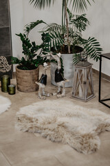 A cozy and stylish indoor corner with lush green potted plants, a vintage lantern with a candle, two decorative duck figurines wearing hats and boots