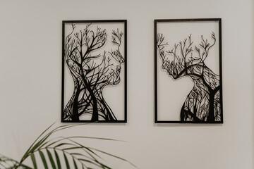 Modern black metal wall art featuring two framed abstract silhouettes of human faces intertwined with tree branches, mounted on a white wall in a contemporary interior with a minimalist aesthetic