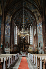 A breathtaking view of a grand Gothic-style church interior with intricate frescoes, towering stained glass windows, and an opulent golden chandelier hanging above the altar