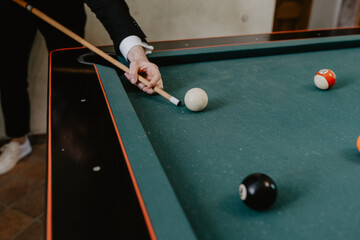A well-dressed man in a suit playing billiards, carefully aiming with a cue stick to hit the cue ball on a green pool table, creating an elegant