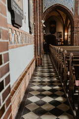 A beautifully captured historic church interior showcasing an aisle with a black and white checkered tile floor, intricate brickwork, wooden pews