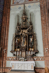  A beautifully crafted Gothic-style church altar featuring intricate wood carvings, religious statues, golden details, and an elegant display of candles and floral decorations