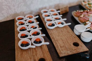 A beautifully arranged catering display featuring small white ceramic spoons filled with fresh blueberries and sliced strawberries