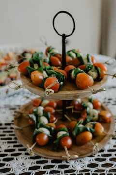 A beautifully arranged two-tiered wooden serving stand displaying caprese skewers made of cherry tomatoes, fresh basil leaves, and mozzarella cheese