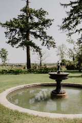  Elegant black tiered fountain in a lush green garden with a stone border, surrounded by towering trees