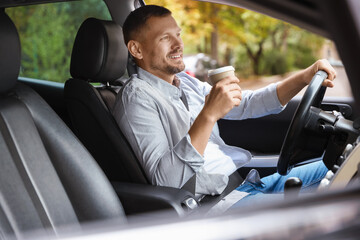 Man with cup of coffee driving modern car