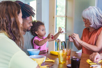 Multigenerational family enjoying breakfast together at home, granddaughter interacts with...