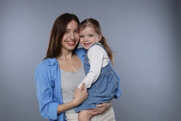 Portrait of happy mother with her cute little daughter on grey background
