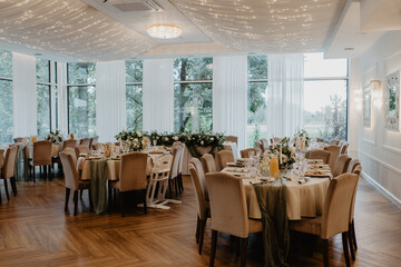 A luxurious wedding reception hall elegantly decorated with round tables draped in white tablecloths, plush upholstered chairs, floral centerpieces, soft green table runners