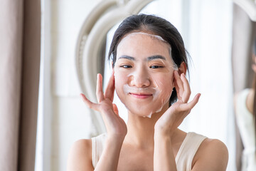 Naklejka premium Young Asian woman applying facial sheet mask for skincare routine