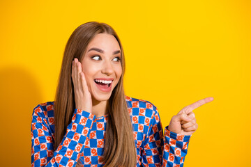 Woman pointing to the side with excitement against a vibrant yellow backdrop showcasing casual...