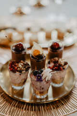 A beautifully presented assortment of gourmet dessert cups arranged on a golden tray, featuring layered chocolate and berry mousse topped with fresh fruit, edible flowers, and delicate chocolate 