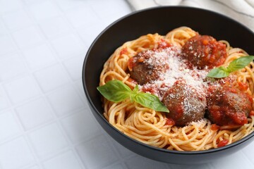 Delicious pasta with meatballs and cheese in bowl on white tiled table, closeup. Space for text