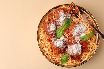 Delicious pasta with meatballs, cheese and basil in bowl on beige table, top view. Space for text