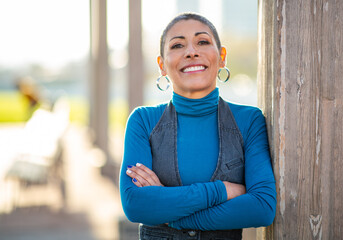 Middle aged woman smiling confidently while leaning on a wooden pillar