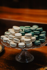  Elegant display of assorted French macarons in shades of white and green, artfully arranged on a vintage glass cake stand in a warm, rustic setting, perfect for weddings, celebrations, and high-end 