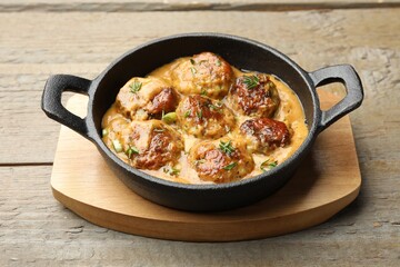 Delicious meatballs with gravy cream sauce and herbs on wooden table, closeup