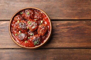 Delicious meatballs with tomato sauce and herbs on wooden table, top view. Space for text
