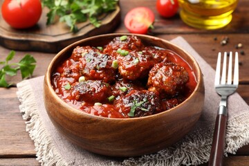 Delicious meatballs with tomato sauce and herbs served on wooden table, closeup