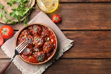 Delicious meatballs with tomato sauce and herbs served on wooden table, flat lay. Space for text