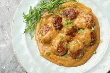 Delicious meatballs with gravy cream sauce, herbs and arugula on grey table, top view