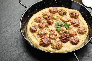 Delicious meatballs with gravy cream sauce and herbs on black table, closeup