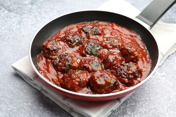 Delicious meatballs with tomato sauce and herbs in on grey table, closeup
