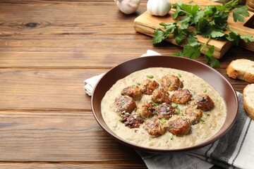 Delicious meatballs with gravy cream sauce and herbs served on wooden table. Space for text