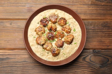 Delicious meatballs with gravy cream sauce and herbs on wooden table, top view