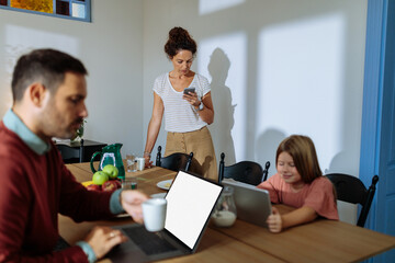 Family sitting at dining table and using electronics