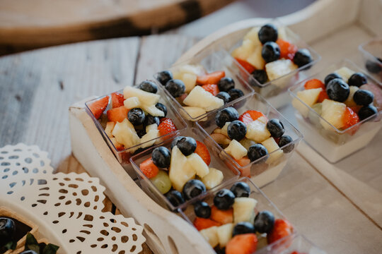  A beautifully arranged selection of fresh fruit salad cups served in small transparent containers, featuring a colorful mix of blueberries, strawberries, pineapple, and grapes
