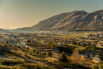 Obraz premium A breathtaking mountain valley with scattered houses bathed in golden sunlight. The rural landscape reflects a peaceful, remote lifestyle, ideal for nature, real estate, tourism.