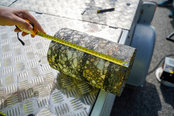 Close-Up of Cylindrical Core Cut from Asphalt Road with Worker Measuring and Evaluating Paving Layers