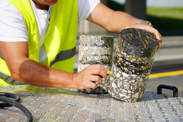 Worker Using Colored Chalk to Mark and Place Number on Cylindrical Core Sample from Asphalt Road
