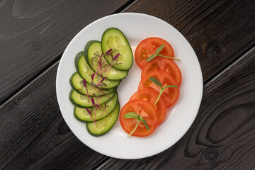 Sliced cucumber and tomatoes on a white plate, garnished with microgreens