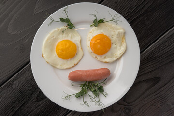 A simple breakfast plate with two fried eggs and a sausage, with microgreens on a white plate.