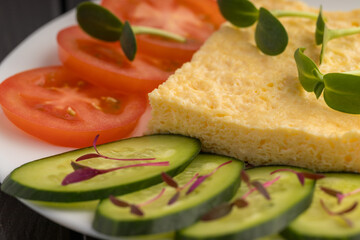 Close-up of an omelette with sliced cucumber, tomatoes, and microgreens on a white plate