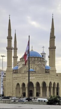 Beirut, Lebanon 01 26 2025: Al Amin mosque with blue domes and Christian church with a cross in downtown Beirut. Lebanese flag prominent. Diversity, religious coexistence, national identity. Vertical