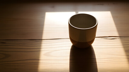 Sunlit Ceramic Cup: A minimalist photograph of a handcrafted ceramic cup sitting on a rustic wooden table, bathed in warm sunlight streaming through a window.