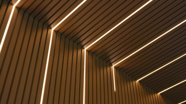 Modern interior design featuring ceiling and walls with wooden slats and integrated linear LED lighting. Lights create geometric pattern that adds contemporary look