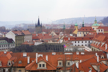 Obraz premium A cityscape with red-tiled rooftops, historic buildings, and church spires under an overcast sky