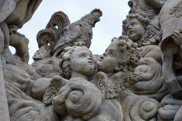 A detailed stone sculpture features cherubs with curly hair and delicate wings, surrounded by intricate carvings, including a rooster and other decorative elements