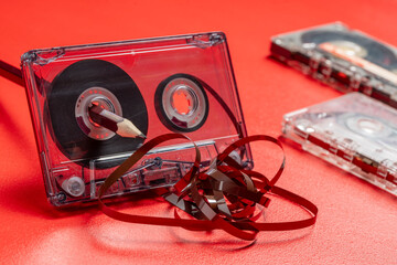Rewinding magnetic tape in a cassette manually with a pencil on a red background, closeup. Old methods of rewinding music tapes, vintage style