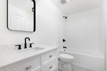 A white bathroom with a grey hexagon tile floor, black mirror and faucet, and a white tiled shower.