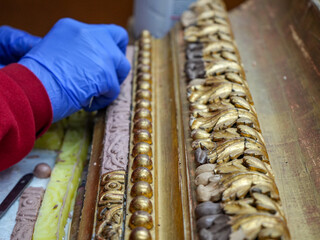 Detail of a gold leaf frame being restored by a professional with latex gloves.