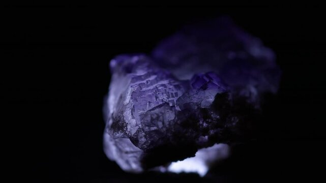 Close up of natural purple fluorite stone illuminated rotating black background