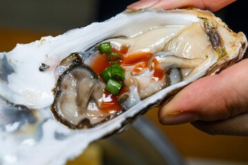 raw oyster with green onion and hot sauce on the hand