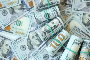 Many rolls of one hundred dollar bills lies on big amount of american currency banknotes
