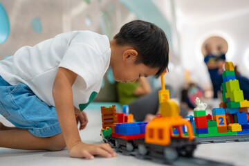 Little asian kindergarten boy enjoy and learnning play toy train block on white room