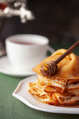 Pancakes or crepes in a plate with honey and tea